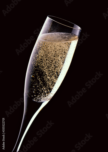 An image of a tilted fluted glass with fizzy champagne on a black background