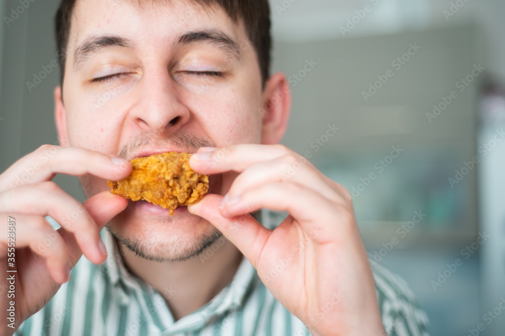 Man eat spicy chicken. Hot chicken wings, guy bites off spicy chicken with eyes closed Man eat spicy chicken. Hot chicken wings, guy bites off spicy chicken with eyes closed