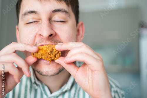 Man eat spicy chicken. Hot chicken wings, guy bites off spicy chicken with eyes closed