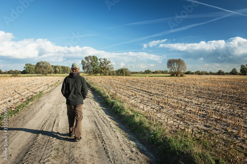 A man walking through a dirt road, fields and blue sky