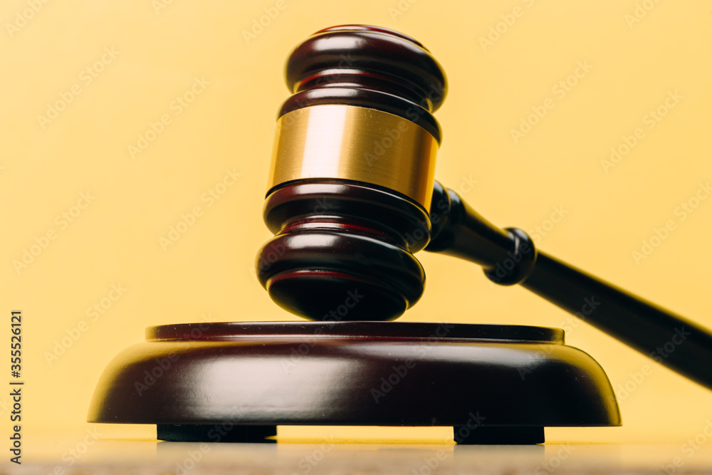 Judge Gavel on a wooden table and yellow-orange background.