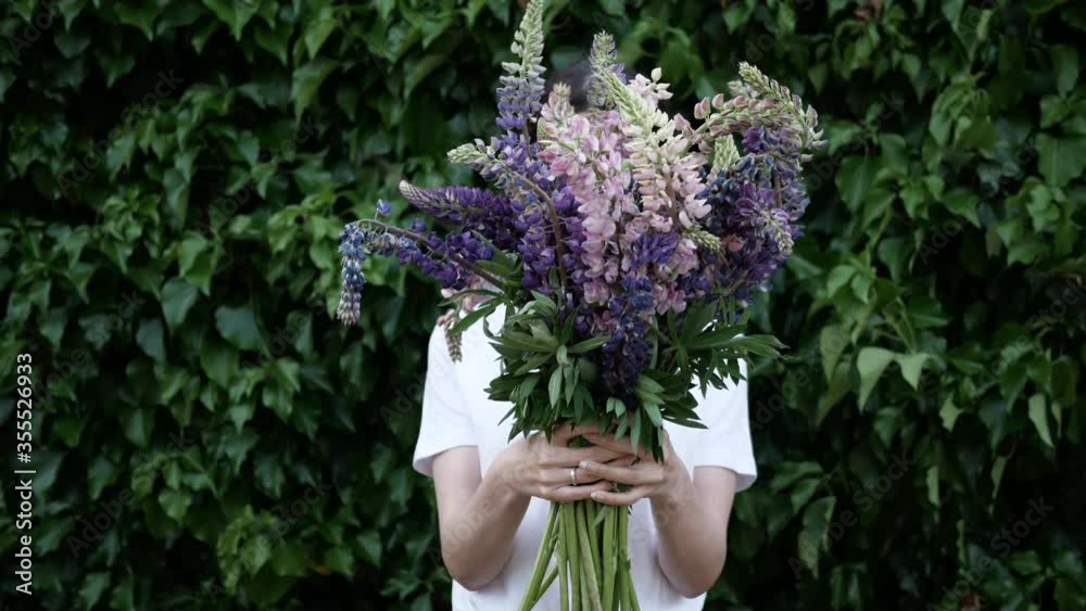 Beautiful bouquet of flowers in hands of a young woman holding it in front of him on background of green plant wall Beautiful bouquet of flowers in hands of a young woman holding it in front of him on background of green plant wall