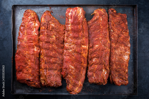 Raw pork spare loin ribs St Louis cut with spicy rub offered as top view on an old rustic metal tray on black background