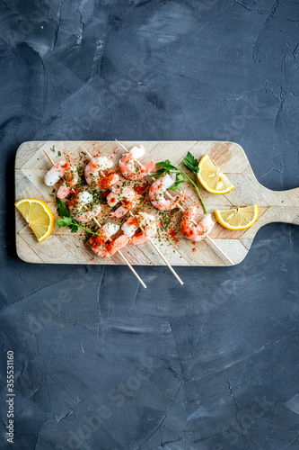 Shrimp skewers - seafood snack - on cutting bioard on grey table top view copy space photo