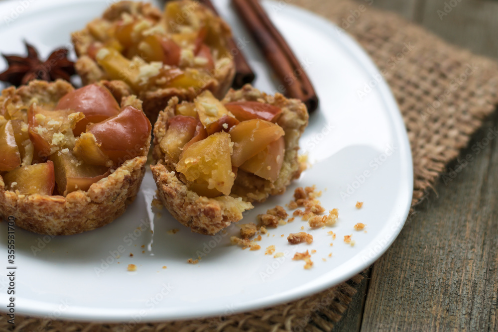 Crispy small tartlets made from shortcrust pastry with apples, homemade sweets with anise and cinnamon. Top view, gunny on a wooden background. Rustic style. Eco sweets concept, warm cozy tea party