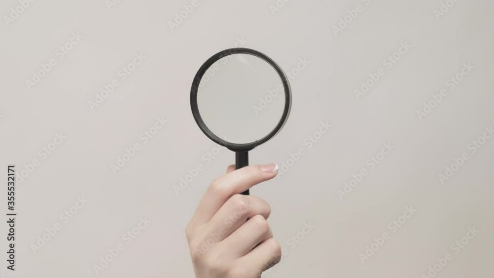 Hand gestures. Promotional background. Woman exploring empty space with magnifying glass isolated on gray. Hand gestures. Promotional background. Woman exploring empty space with magnifying glass isolated on gray.