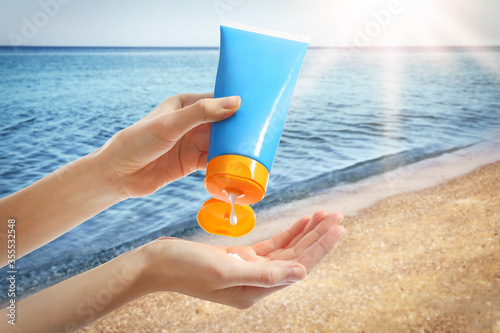 Young woman applying sun protection cream near sea, closeup