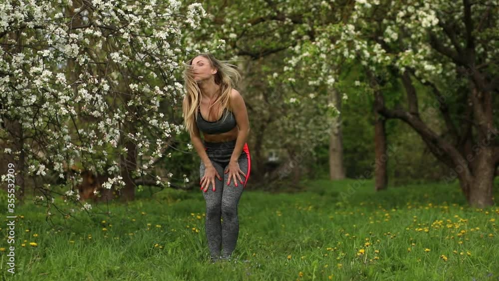 Athletic woman is doing warming up, body tilt, stretching and other fitness exercises outdoors in the blooming park. Athletic woman is doing warming up, body tilt, stretching and other fitness exercises outdoors in the blooming park.