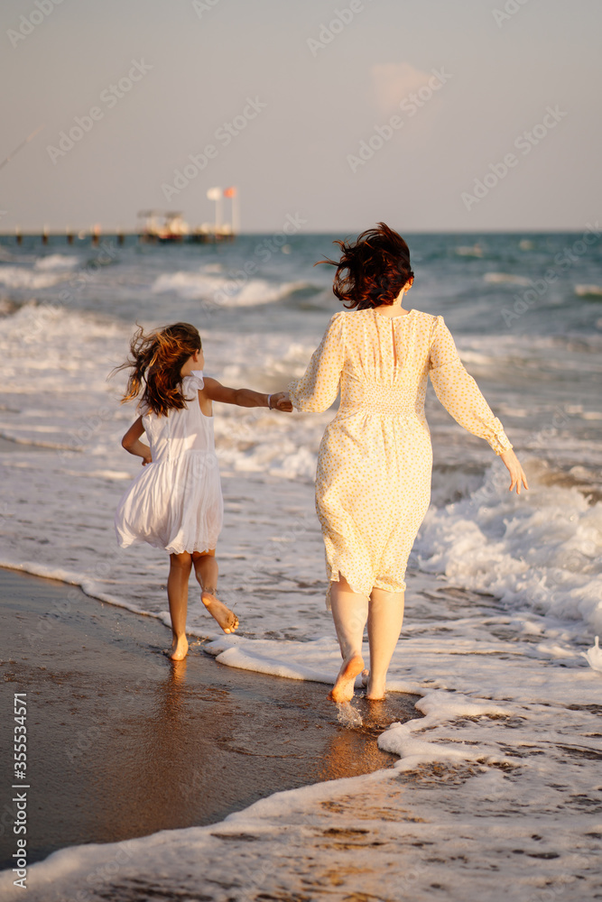 fun mom and kid walking on beach with big waves in windy weather. happy family fun mom and kid walking on beach with big waves in windy weather. happy family
