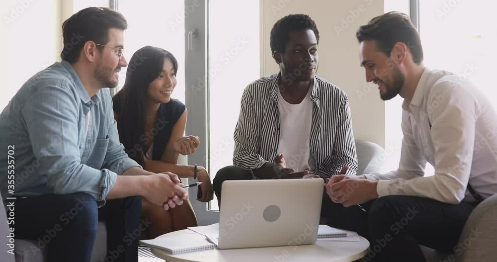 Friendly happy multiethnic business team working together discussing corporate project plan with laptop, diverse smiling workers group brainstorming talking gathered in office at teamwork meeting