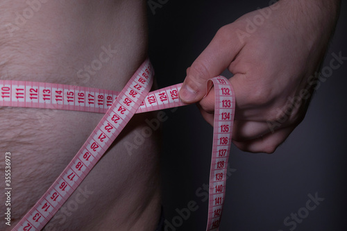 male hand measures male waist with red tape measure. Diet and weight loss concept. High quality photo