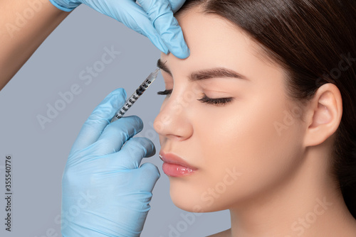 Cosmetologist does injections in the wrinkles between the eyebrows and on the face of a beautiful woman in a beauty salon. Women s cosmetology in the beauty salon.