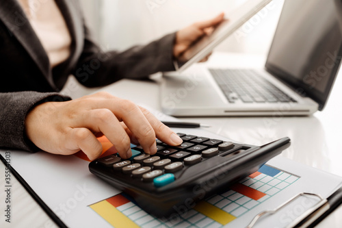 Businesswomen hands working with finances about cost and calculator and laptop with tablet, smartphone at office in morning light