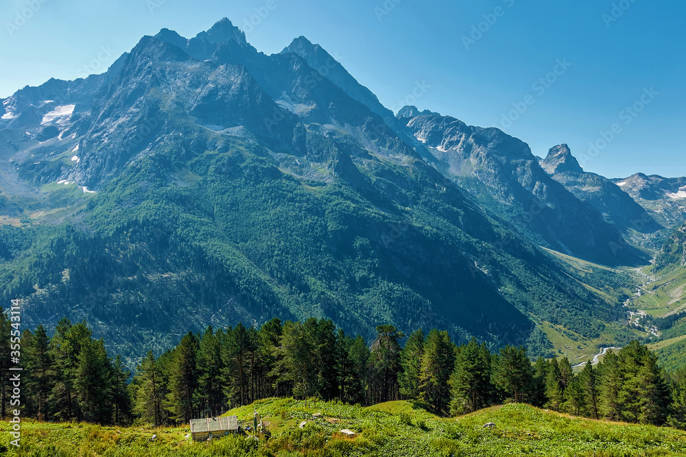 Hilly mountains against a cloudless blue sky. Snowy peaks. Coniferous forest in the foreground and the river in the distance. Tourism, travel, climbing, mountaineering.