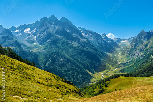 Hilly mountains against a cloudless blue sky. Snowy peaks. Coniferous forest in the foreground and the river in the distance. Tourism, travel, climbing, mountaineering. trek