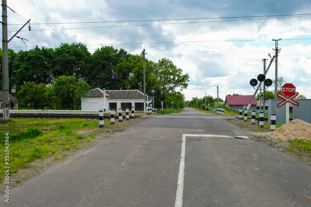 Empty railway crossing with a warning sign stop and a traffic light in a Ukrainian village before the rain. Copy space.