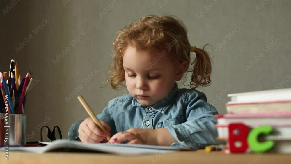 Girl schoolboy with two ponytails in glasses sits on desk harming textbooks and writes on paper, back to school Girl schoolboy with two ponytails in glasses sits on desk harming textbooks and writes on paper, back to school