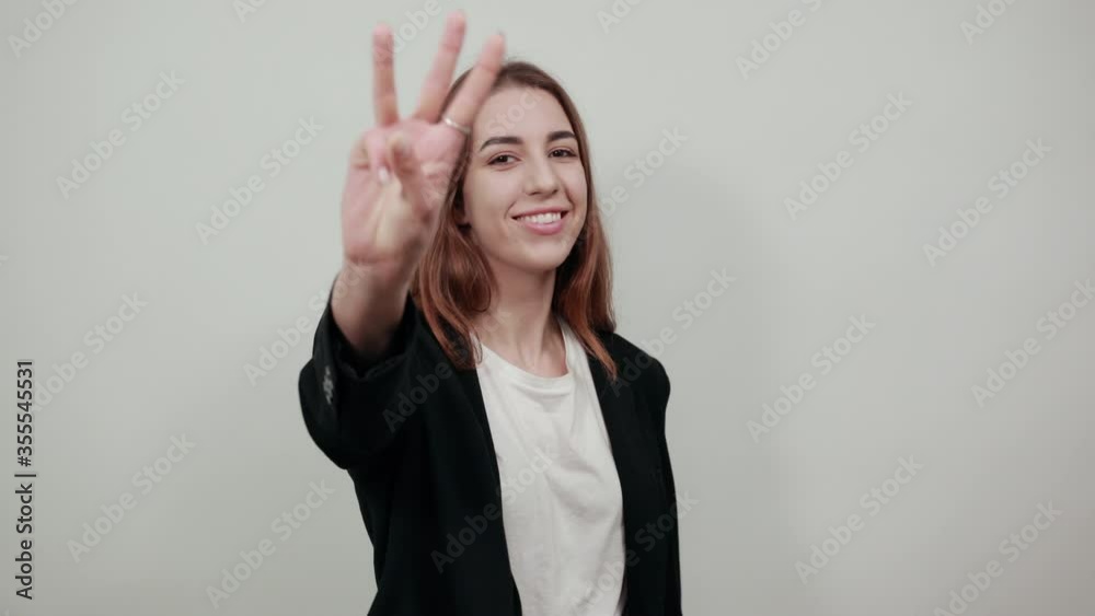 Young attractive woman with brown hair in a light t-shirt and black jacket on white background. Happy female smiles shows three fingers, account, business, demonstrates