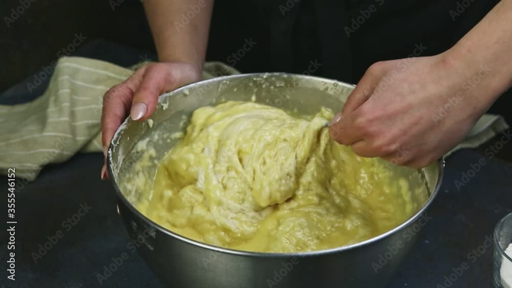closeup female hands slowly mixing by spoon soft yeast dough in deep metal bowl closeup female hands slowly mixing by spoon soft yeast dough in deep metal bowl