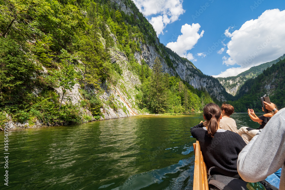 Tourists on a wooden tourboat taking pictures of a waterfall (Traun-Ursprung) splashing into Lake Toplitz, Ausseer Land region, Styria, Austria
