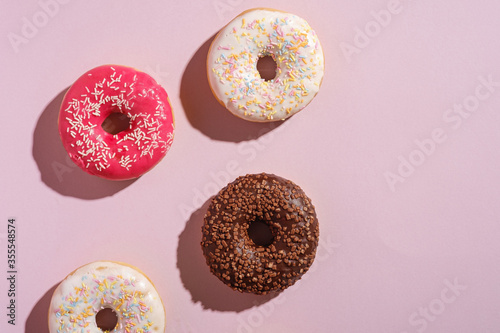 Chocolate, pink and vanilla donuts with sprinkles, sweet glazed dessert food on pink minimal background, top view copy space
