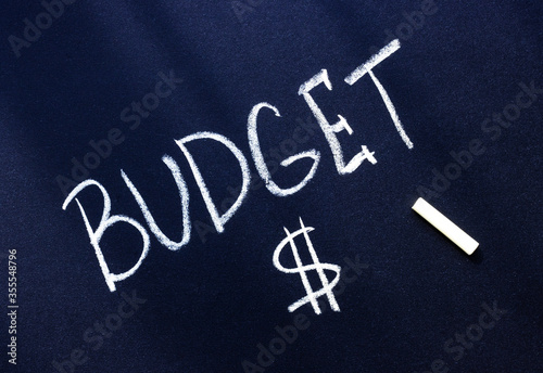 the word budget is written in white chalk on a black surface and a dollar sign