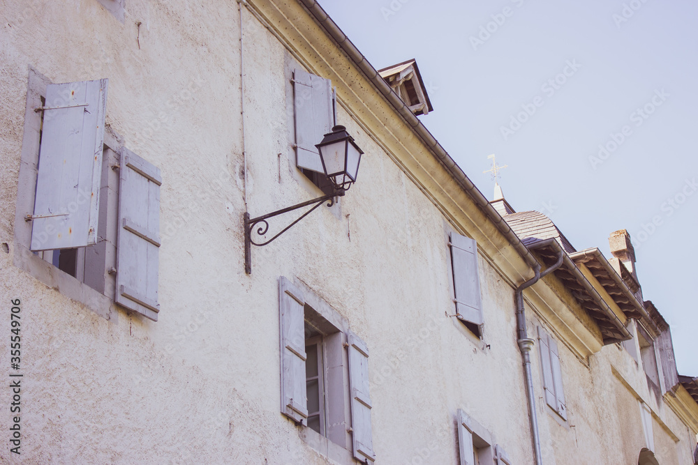 Medieval building with outdoor lamp filtered. Facade of old house with window shutters. Ancient architecture concept. Historic building in village, France. Vintage house with street lantern.