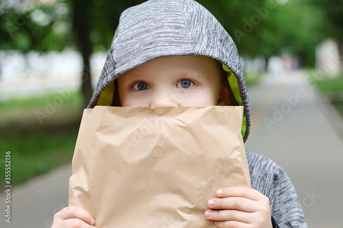 Funny blondheared toddler eating georgian bread with appetite on the street.Holding its in the paper craft package. Closeup photography of funny boy.Copy space for text. photo