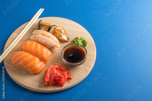 Delicious appetizing nigiri sushi set served on wooden plates with soy sauce and chopsticks. Blue background