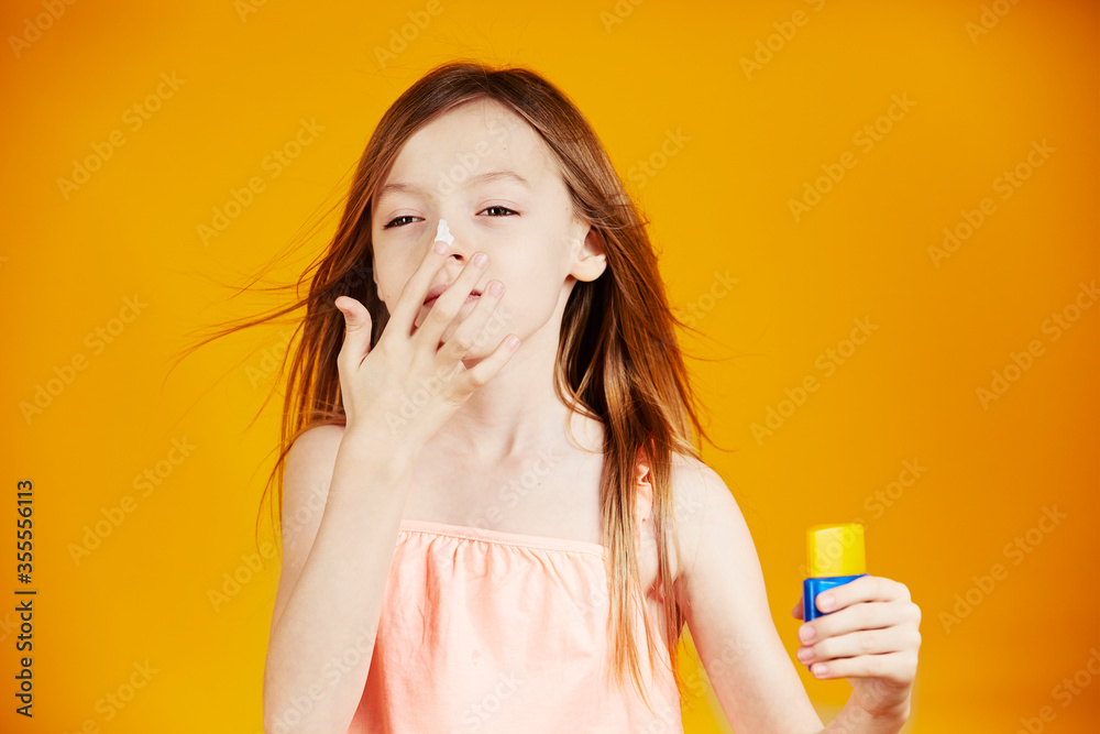 jolie jeune enfant fille caucasienne aux cheveux longs châtains mettant de la crème solaire sur son visage pour protéger sa peau sur fond jaune de studio jolie jeune enfant fille caucasienne aux cheveux longs châtains mettant de la crème solaire sur son visage pour protéger sa peau sur fond jaune de studio