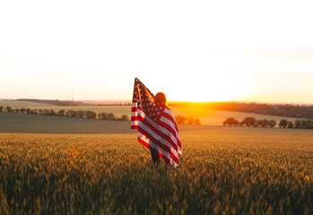 Beautiful girl with the American flag in a wheat field at sunset. 4th of July.  Independence Day.
