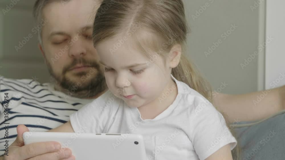 Dad tries not to sleep while playing with his daughter. Kid having fun and laughing using tablet. Funny games app. Dad tries not to sleep while playing with his daughter. Kid having fun and laughing using tablet. Funny games app.