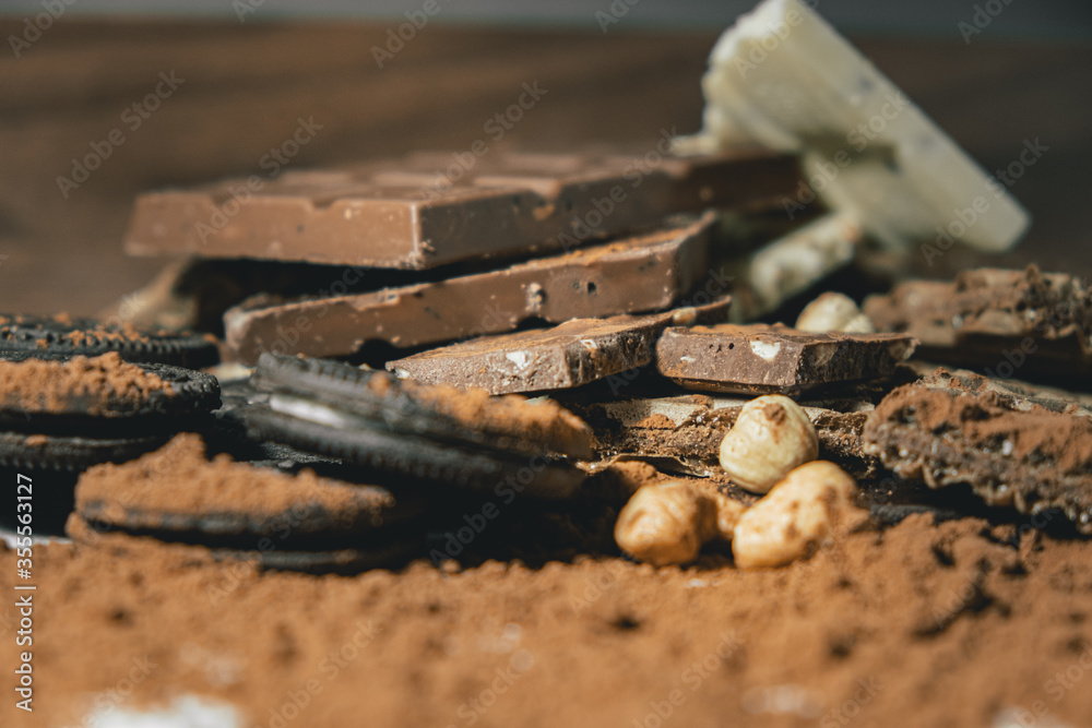 heap of chocolate, round biscuit with toppings, hazelnuts and cashews and faffles. All sprinkled with cocoa. World Chocolate Day.