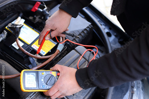 A mechanic/service engineer checking the fuse box of a car with a voltmeter 