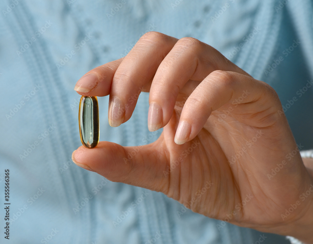 Woman hand holds yellow medication capsules of omega 3, pours from a white bottle into palm the fish oil, healthy supplement pills. Омега 3. Витамин Е