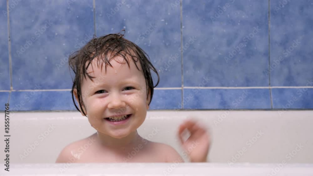 Kid splashing water in bath room. Little happy girl bathes in the