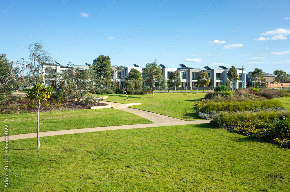 Fototapeta premium A public park with grass and footpath with some modern residential townhouses/Australian homes in the distance. Concept of suburban living, environment and real estate. Melbourne, Australia.