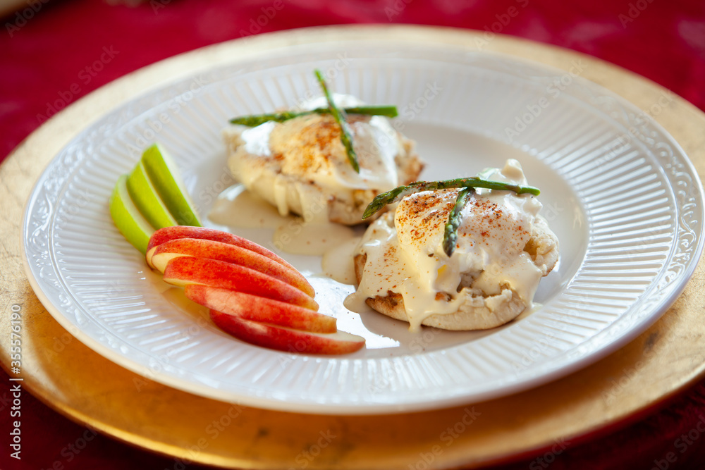 Eggs Benedict breakfast served on English muffins next to sliced apples on a white plate Eggs Benedict breakfast served on English muffins next to sliced apples on a white plate