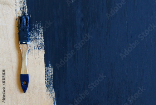 A paint-stained brush lies on a wooden surface, unpainted with dark blue paint . Selective focus. Background
