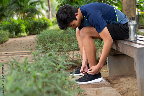 Fotografia asian young fitness man runner sit on the chair park and tying jogging shoes