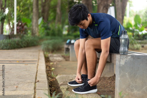 asian young fitness man runner sit on the chair park and tying jogging shoes