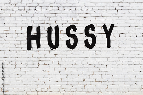 Word hussy painted on white brick wall