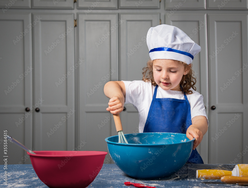 Toddler girl in the kitchen mixing ingredients for baking in big blue bowl Toddler girl in the kitchen mixing ingredients for baking in big blue bowl