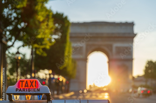 Fototapeta Naklejka Na Ścianę i Meble -  Parisian taxi roof sign in front of the Arc de Triomphe in Paris under a sunset. 
