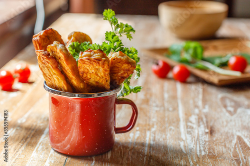 Red enameled cup with fried tempeh or tempe (traditional Indonesian soy product) on wooden surface. Side view. With space. photo