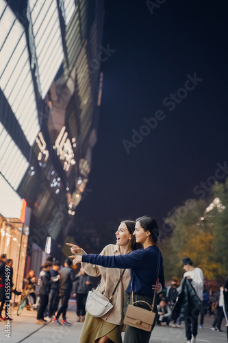 two female friends walking in downtown Beijing at night and looking at something with suprised and shocked faces. two girlfriends exploring China at night