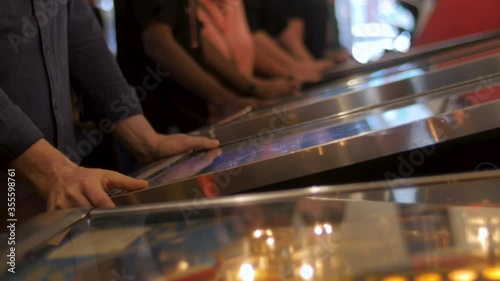 Man playing at a pinball table in a busy arcade