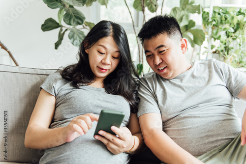 An Asian pregnant woman and her husband are using mobile phones