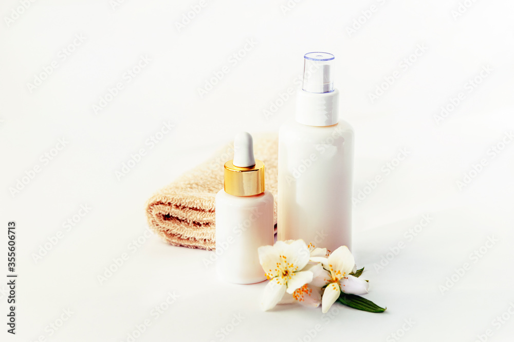Cosmetic tonic and serum unbranded white bottles, towel and jasmine blossom. Spa concept. Cosmetic tonic and serum unbranded white bottles, towel and jasmine blossom. Spa concept.