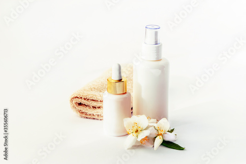 Cosmetic tonic and serum unbranded white bottles, towel and jasmine blossom. Spa concept.